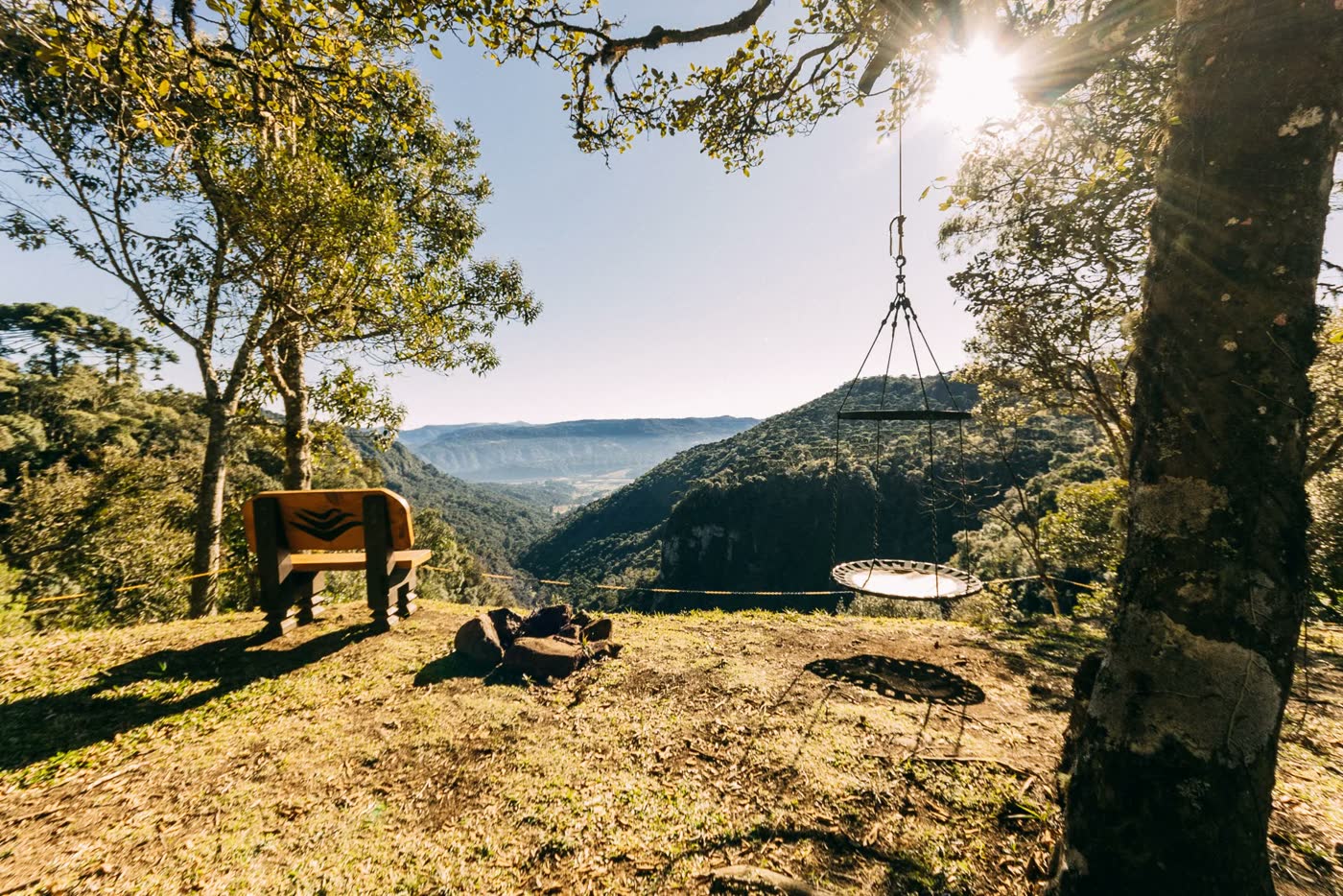 Mirante com bancos e um balanço sob uma árvore, de frente para o vale